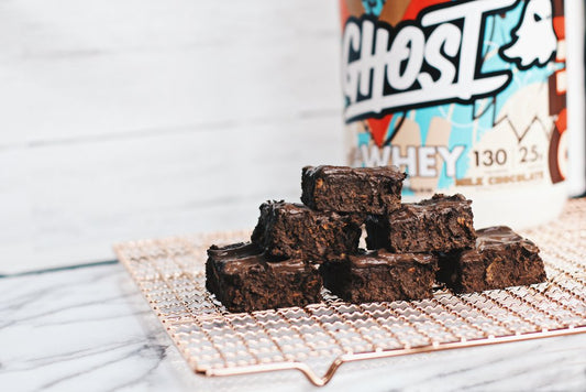 Homemade Chocolate Protein Brownies stacked on a cooling rack next to whey protein powder